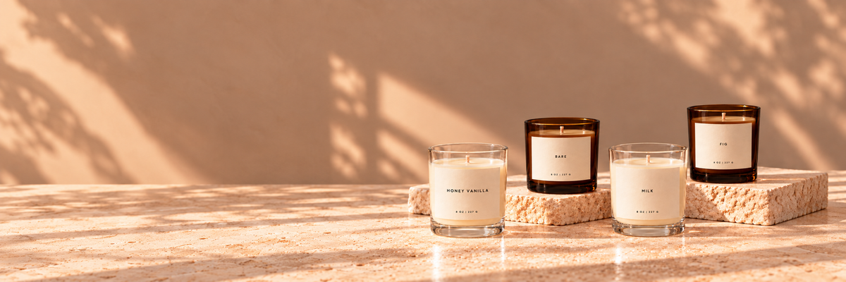 Lije candles in clear and dark amber glass on sunlit travertine, wide composition